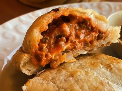 Empanada argentina de massa folhada aberta, com recheio de carne e molho, sobre um prato branco